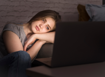 Teenager sitting on a couch late at night, illuminated by the glow of a laptop screen.