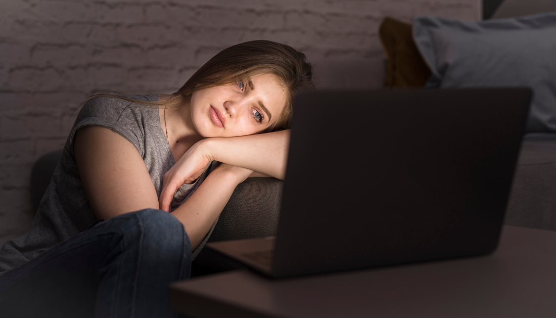 Teenager sitting on a couch late at night, illuminated by the glow of a laptop screen.